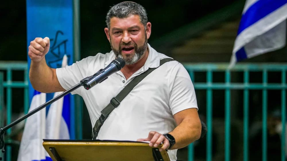 עופר ווינטר נושא דברים מעל במה באירוע, דגלי ישראל ברקע